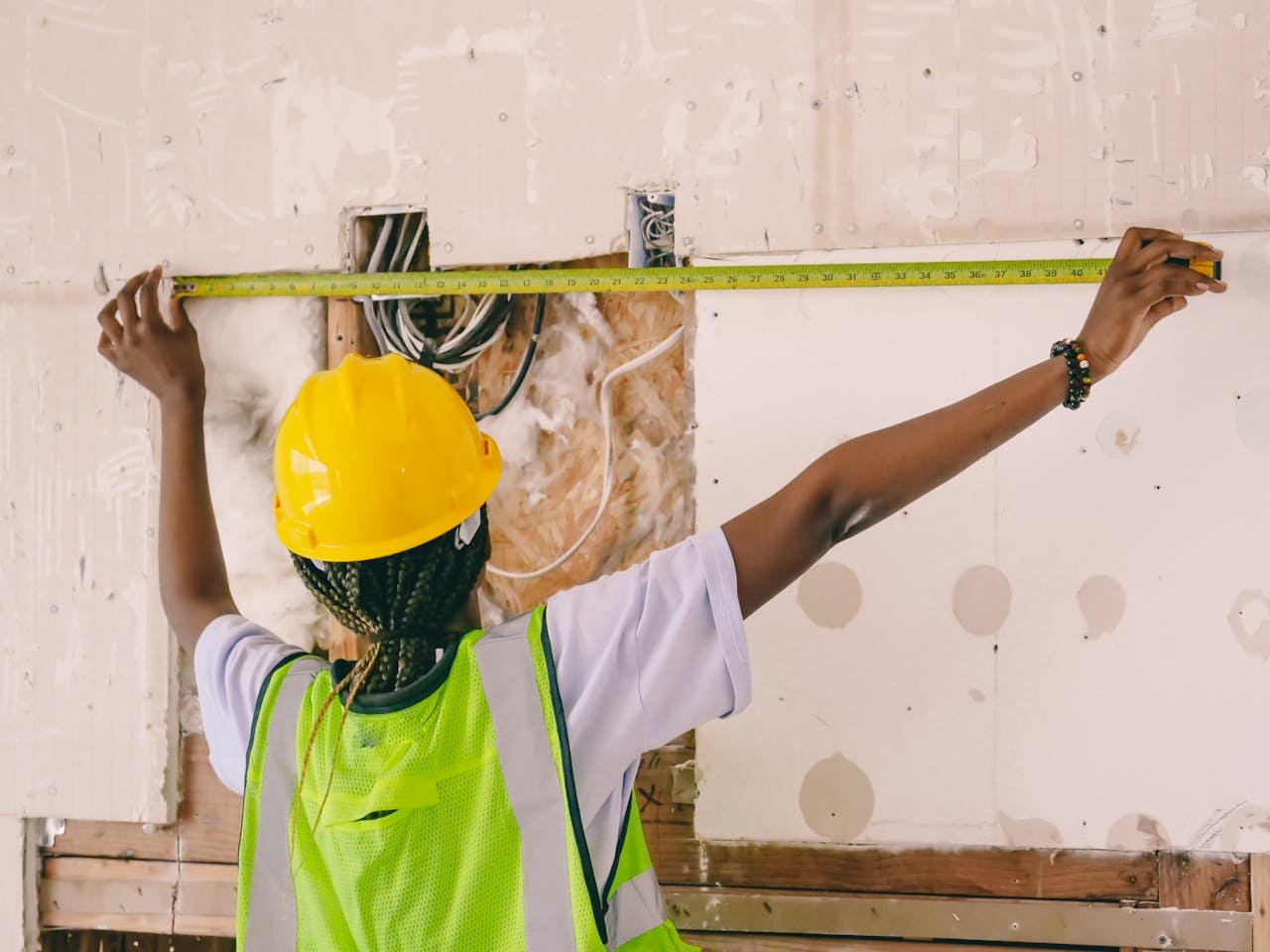 Instalaciones eléctricas en Valencia. Female construction worker with hardhat and vest measuring an interior wall.