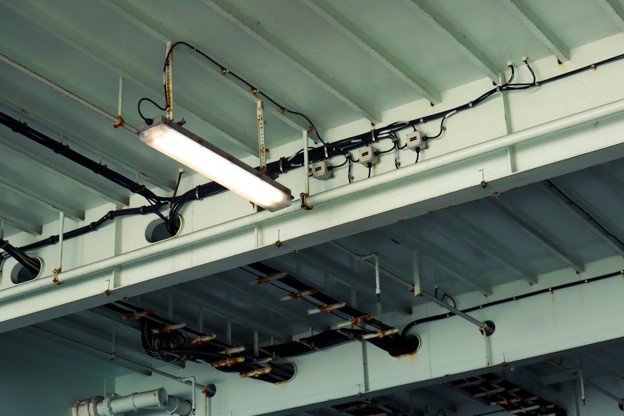 Servicios de Instalaciones eléctricas. Detailed view of industrial ceiling light and wiring at a low angle in an indoor setting.